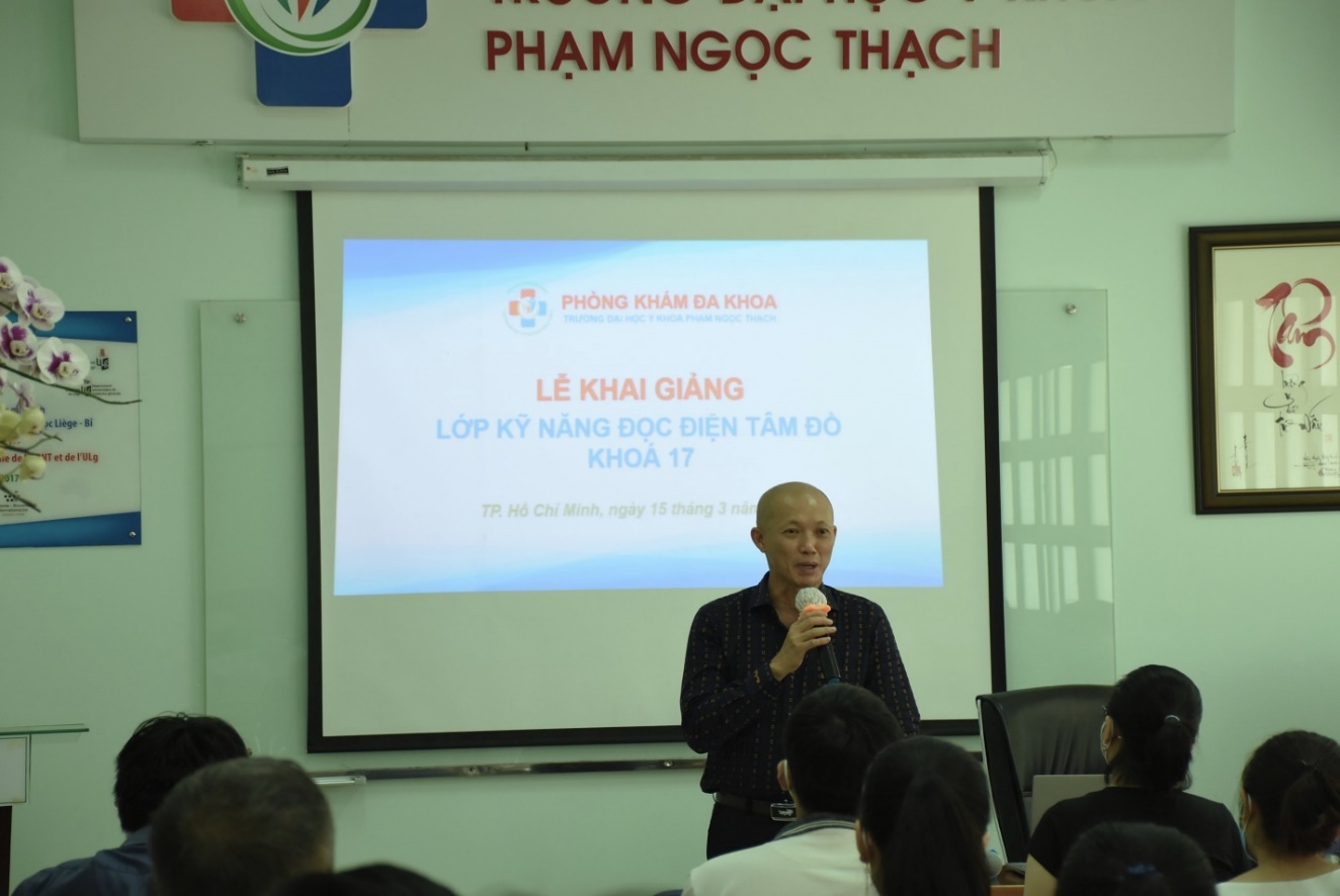 A person speaking into a microphone in front of a group of people Description automatically generated with medium confidence