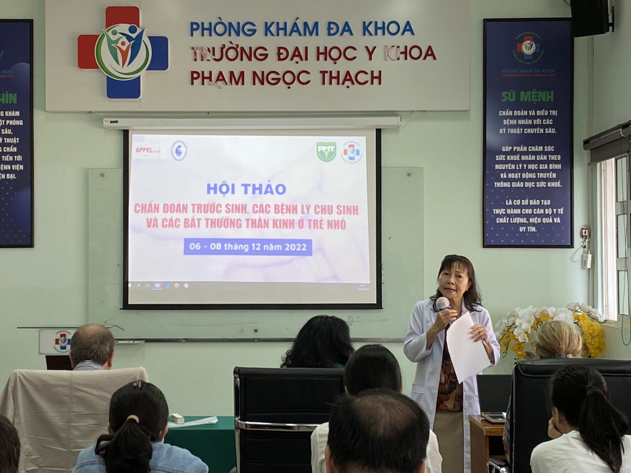 A person speaking to a group of people in a room
Description automatically generated with medium confidence